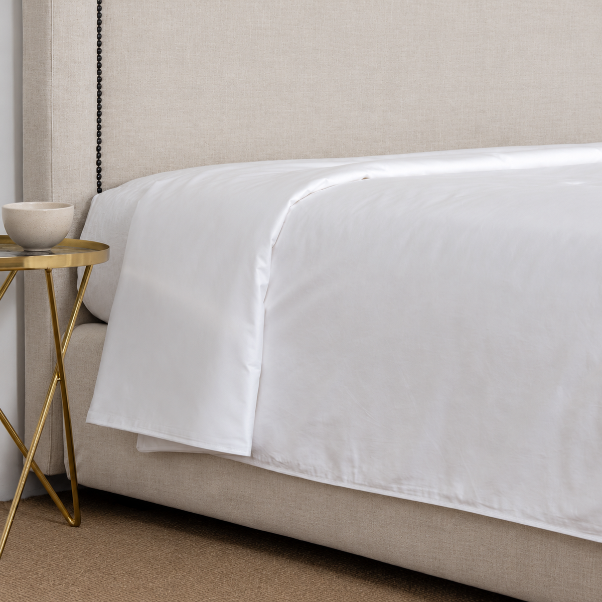 White duvet insert draping over a bed beside an oatmeal headboard and ceramic bowl
